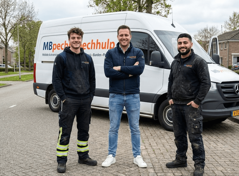 Drie mannen in werkkleding staan glimlachend voor een witte MB Pechhulp servicebus op straat.